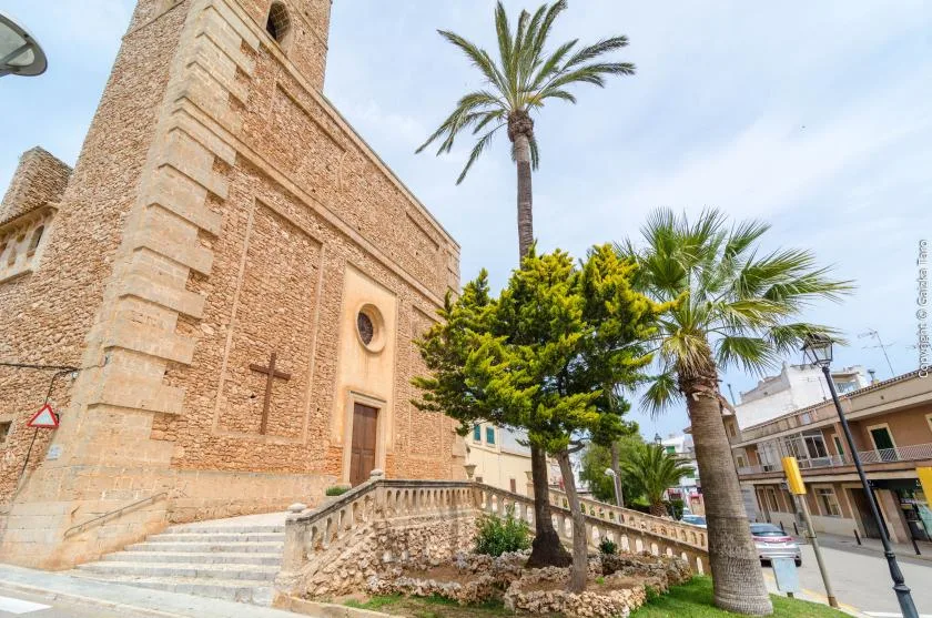 Una iglesia de ladrillo está junto a palmeras y una pequeña plaza ajardinada.