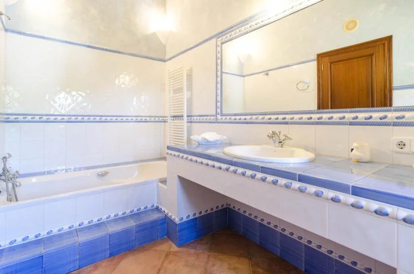 Un baño con azulejos, bañera, lavabo y un espejo grande en la pared.