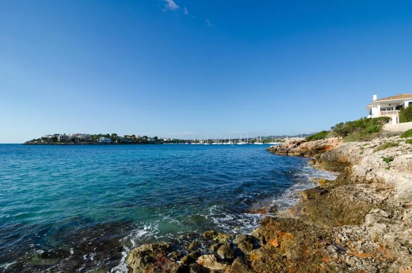 Una costa rocosa bordea aguas azules y claras bajo un cielo soleado.