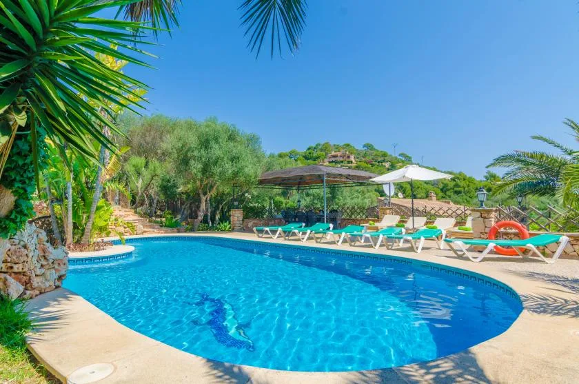 Una piscina con asientos reclinables y sombrillas en un entorno exterior ajardinado.
