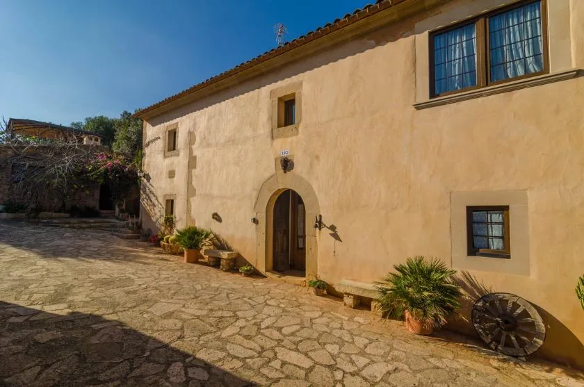 Un patio de piedra soleado junto a un edificio claro con puertas de madera arqueadas.