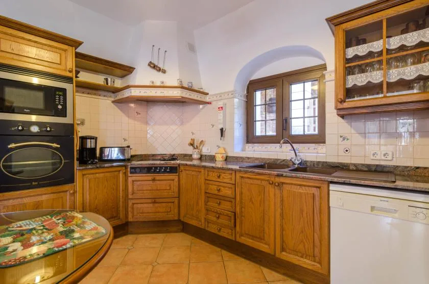 Una cocina de tonos cálidos con armarios de madera, suelo de baldosas y una ventana sobre el fregadero.