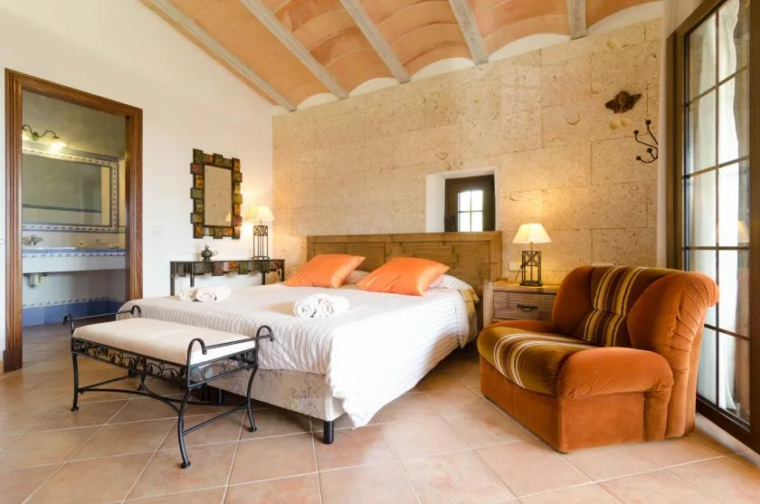 Un dormitorio con una cama doble y un sillón tapizado junto a ventanas altas.