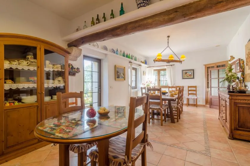 Un comedor con una mesa larga, sillas de madera y un armario con puertas de vidrio.