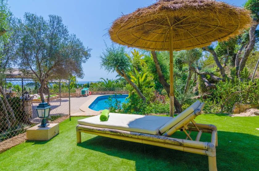 Una zona de descanso junto a la piscina, con una tumbona acolchada bajo una sombrilla de paja.