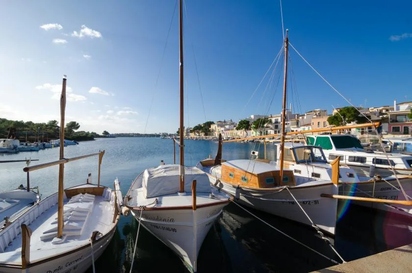 Hay barcos amarrados en una costa soleada, con edificios junto al agua.
