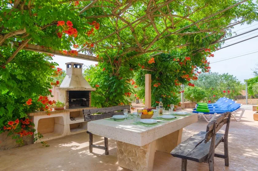 Una zona de comedor al aire libre está bajo una pérgola frondosa junto a una barbacoa empotrada.