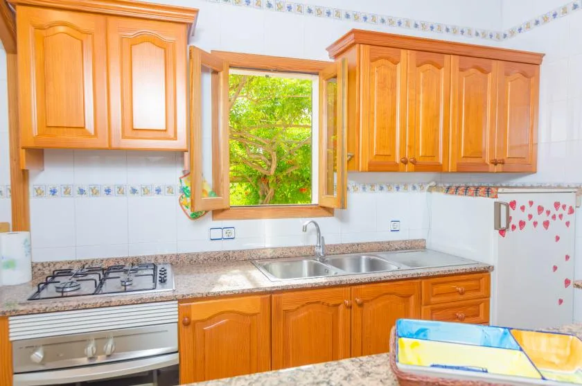 Una cocina luminosa con gabinetes de madera, un fregadero y una ventana abierta.