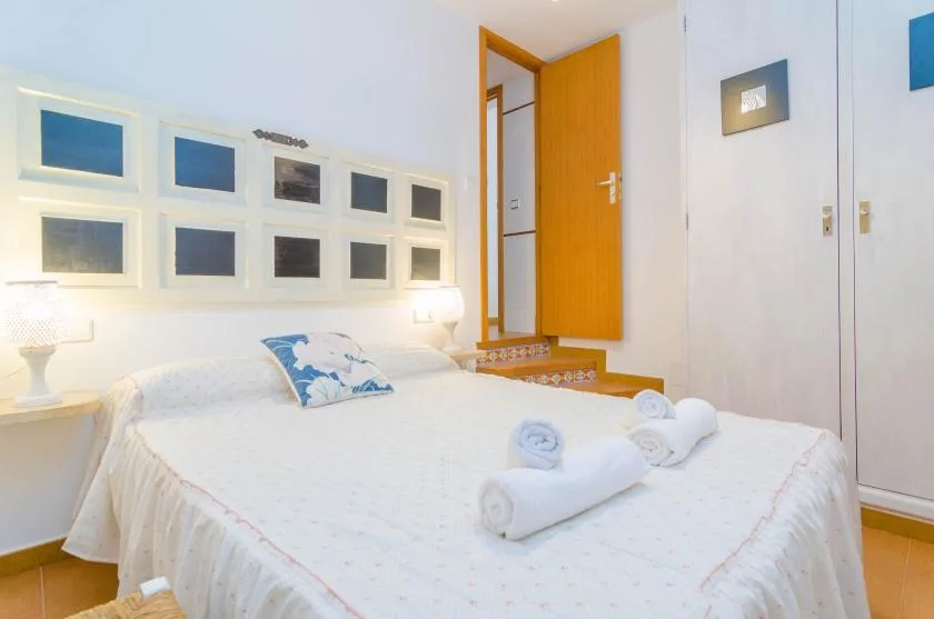 Un dormitorio luminoso con una cama blanca y cuadros en la pared.