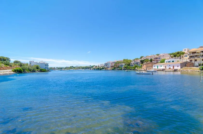 Una amplia zona costera azul se extiende entre edificios bajos bajo un cielo despejado.