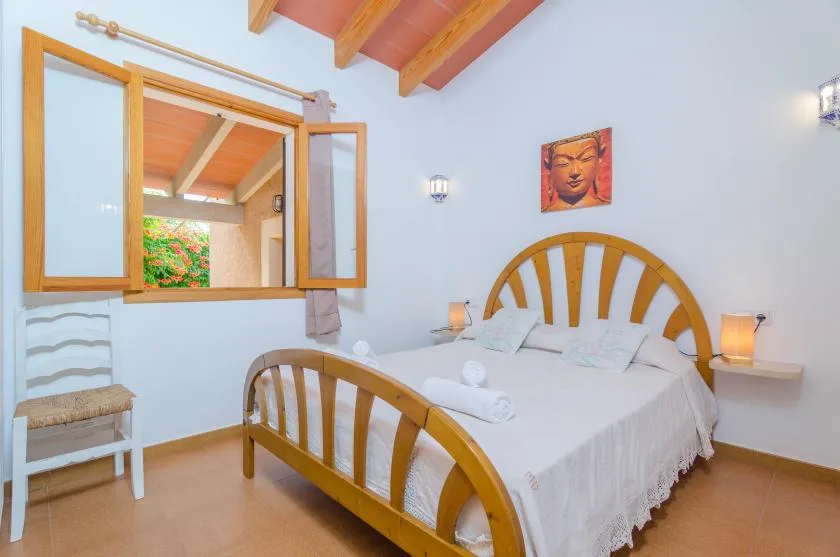 Un dormitorio con una cama de madera, ropa de cama blanca y una ventana abierta.