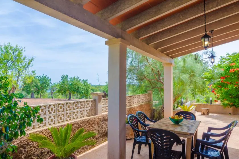 Un patio exterior cubierto con mesa y sillas da a un jardín frondoso.