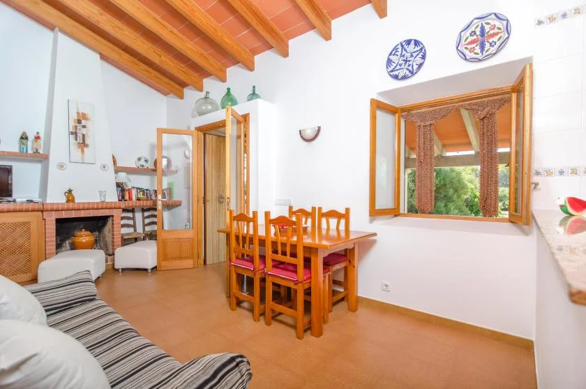 Un comedor con asientos de madera bajo vigas vistas, junto a una ventana abierta.
