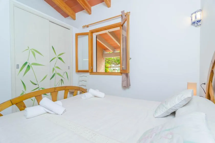 Un dormitorio luminoso con una cama, toallas dobladas y una ventana con vista a la vegetación.