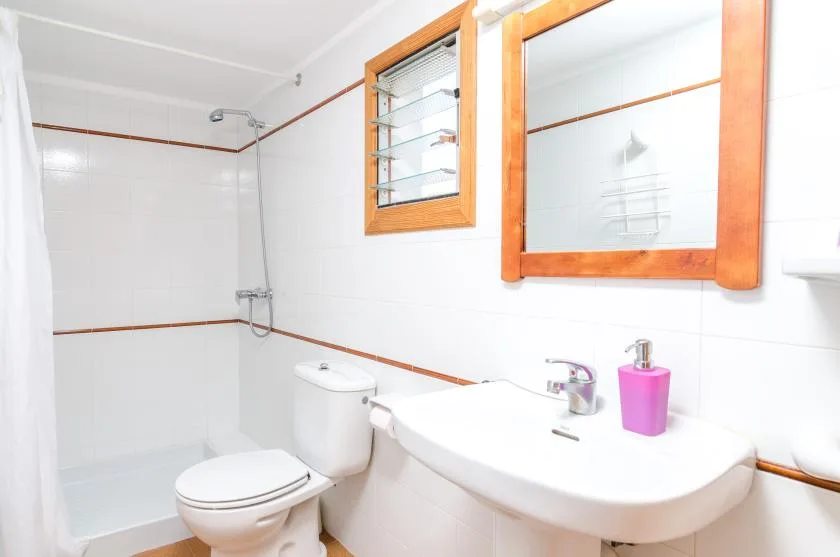 Un baño luminoso con ducha, inodoro y lavabo.