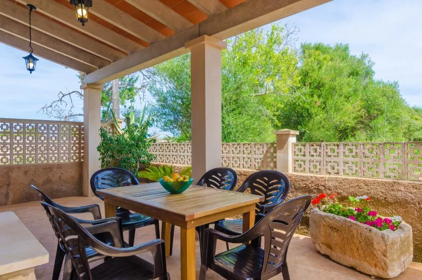 Un patio exterior cubierto tiene una mesa de comedor, asientos y plantas en macetas.