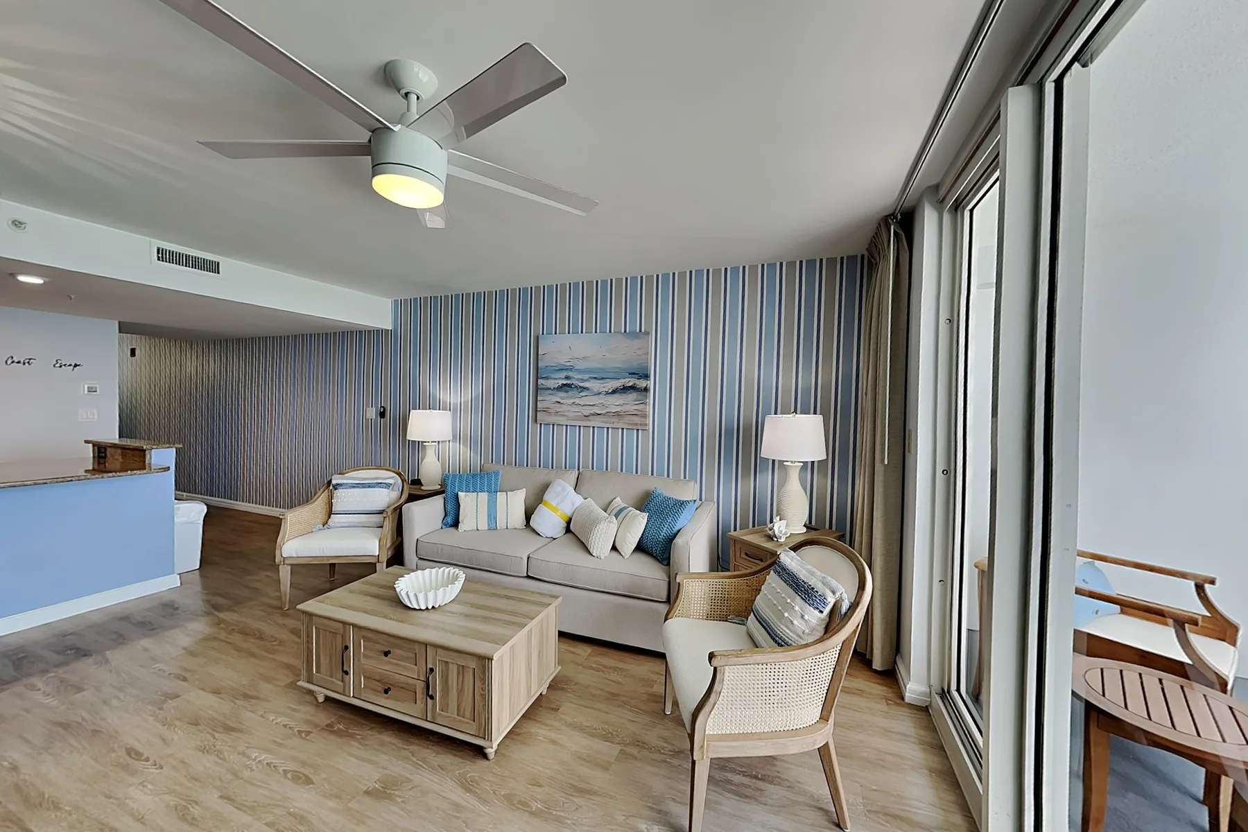 A bright living room with striped walls, seating, and large windows.
