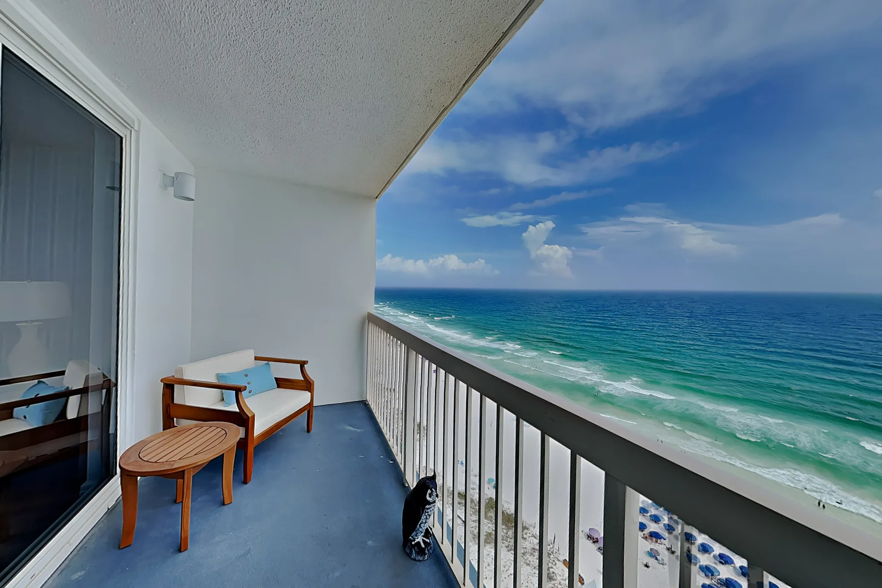 A balcony with seating overlooks the ocean and a sandy beach.