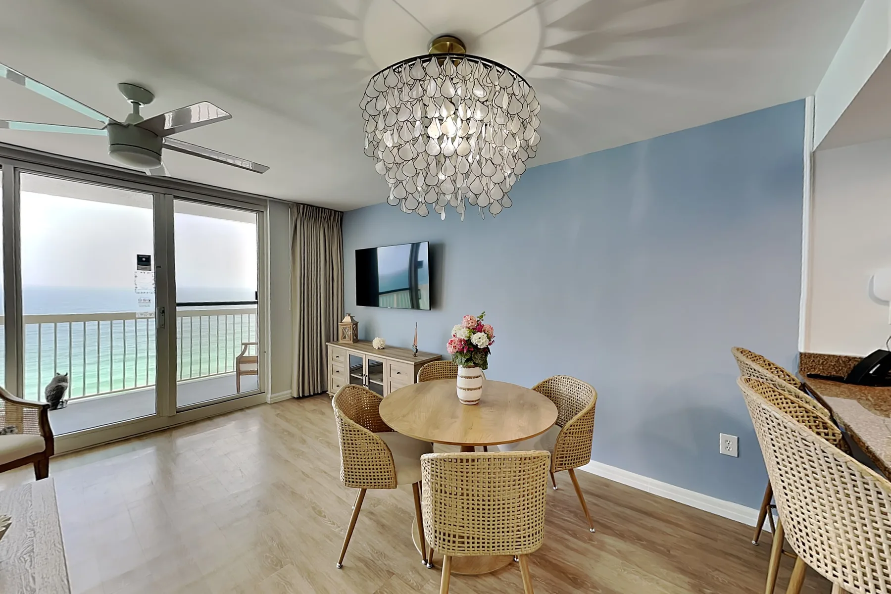 A dining area with a round table and chairs beside large windows overlooking the water.