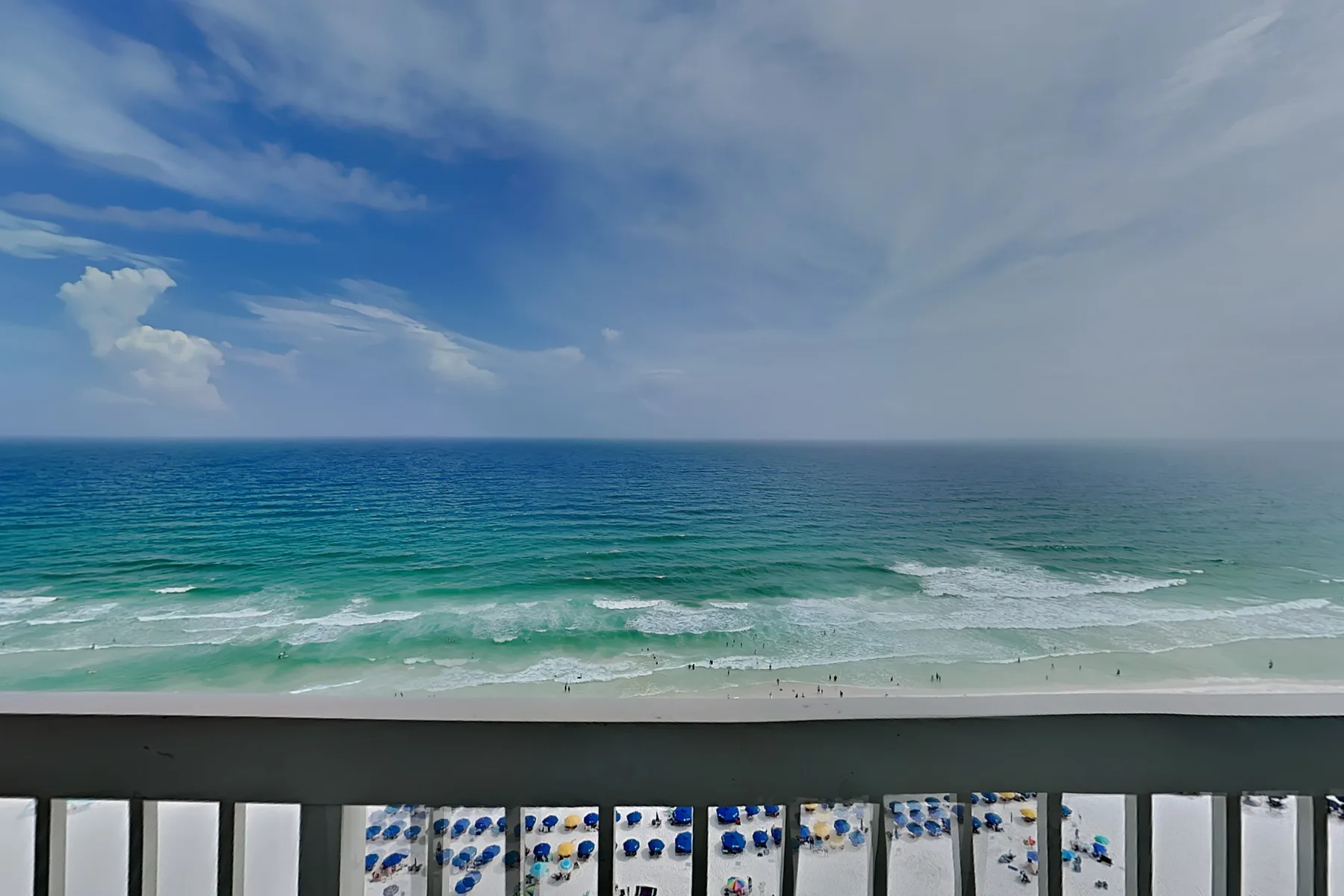 A beach and turquoise waves are visible beyond a balcony railing.