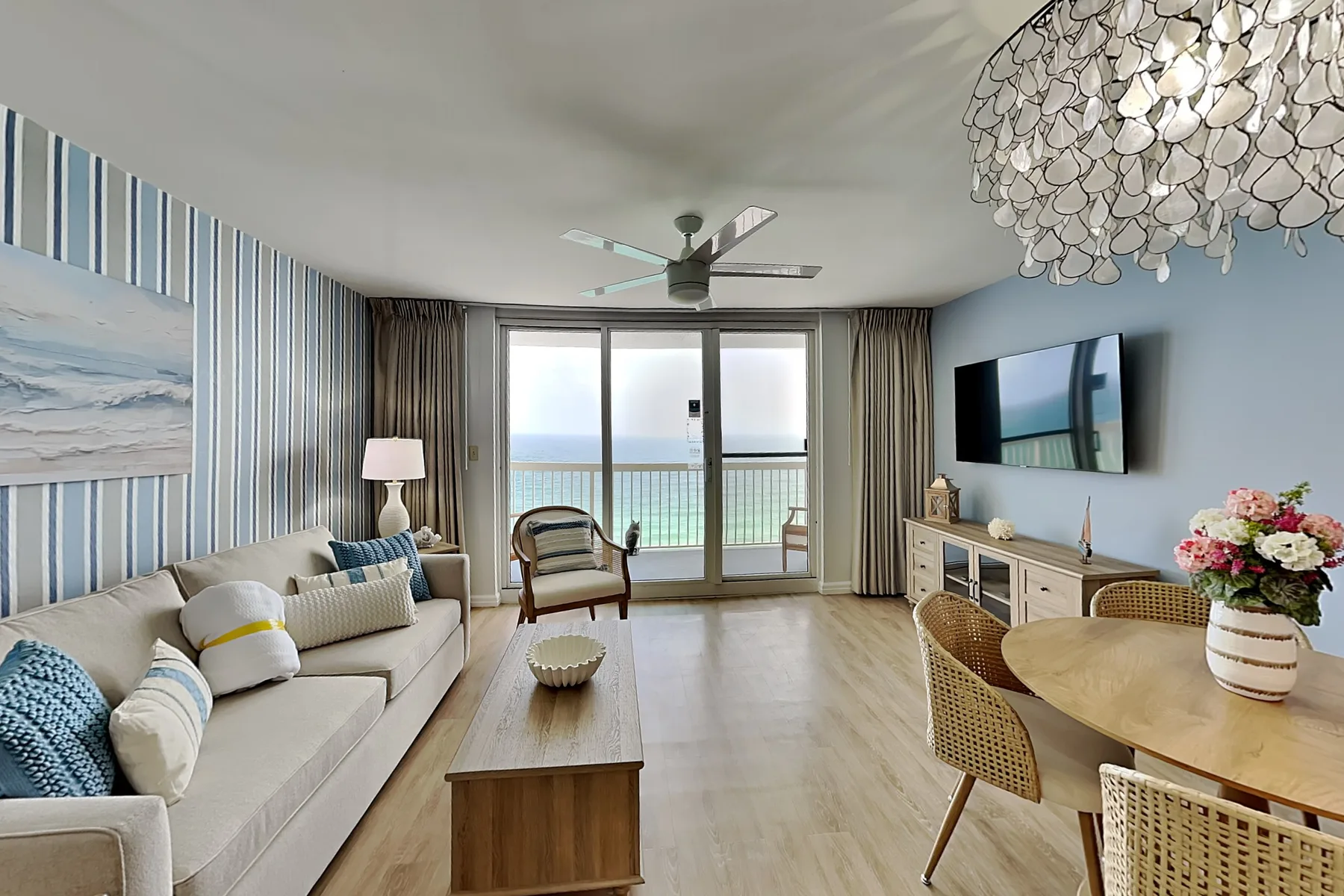 A living and dining area with seating, a television, and glass doors opening to a balcony.