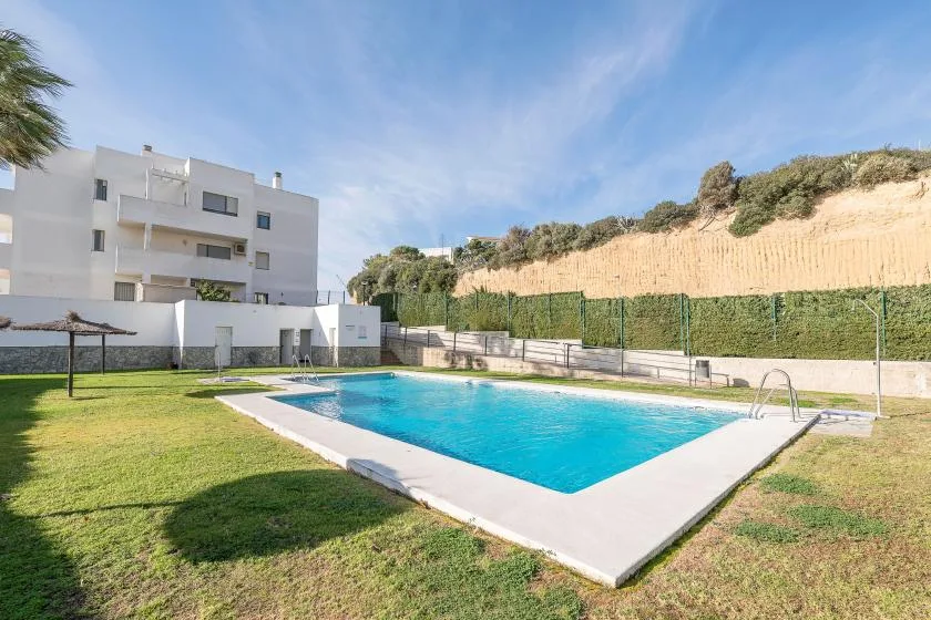 Una piscina al aire libre junto a un edificio de apartamentos blanco y un césped.
