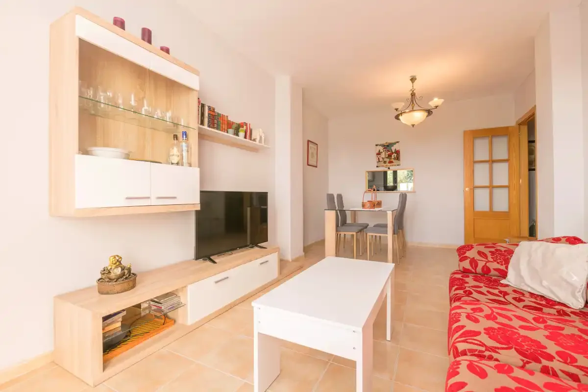 Una sala de estar con televisor, mesa de centro y zona de comedor.