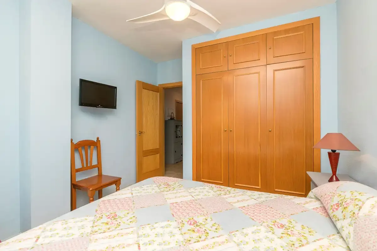 Un dormitorio con una cama, un armario de madera y un televisor en la pared.
