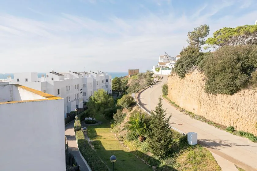 Un camino pavimentado pasa entre edificios blancos y vegetación, en dirección a la costa.