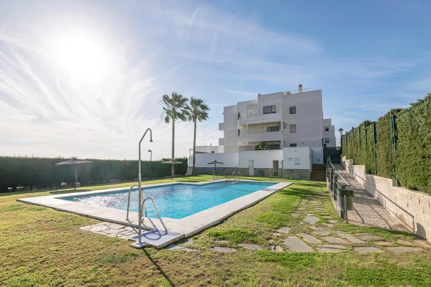 Una piscina al aire libre está junto a un edificio blanco moderno y un camino pavimentado.