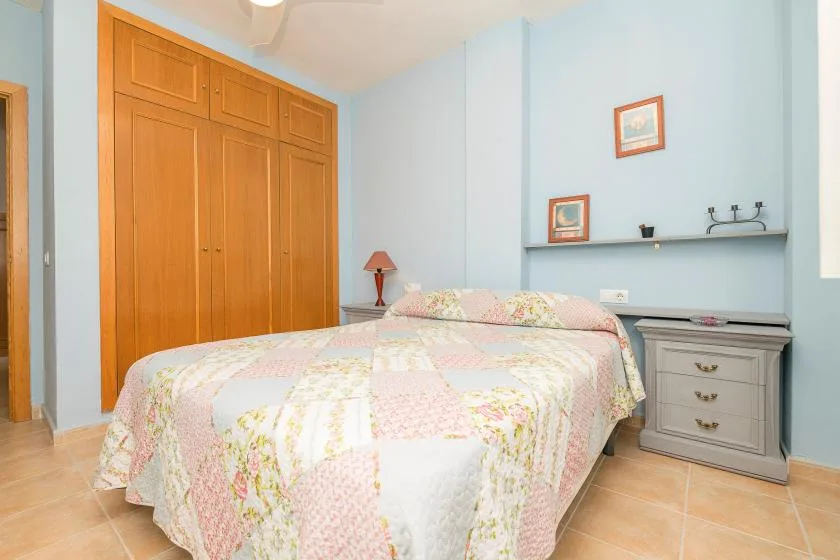 Un dormitorio con una cama cubierta con una colcha floral en tonos pastel y un armario de madera.