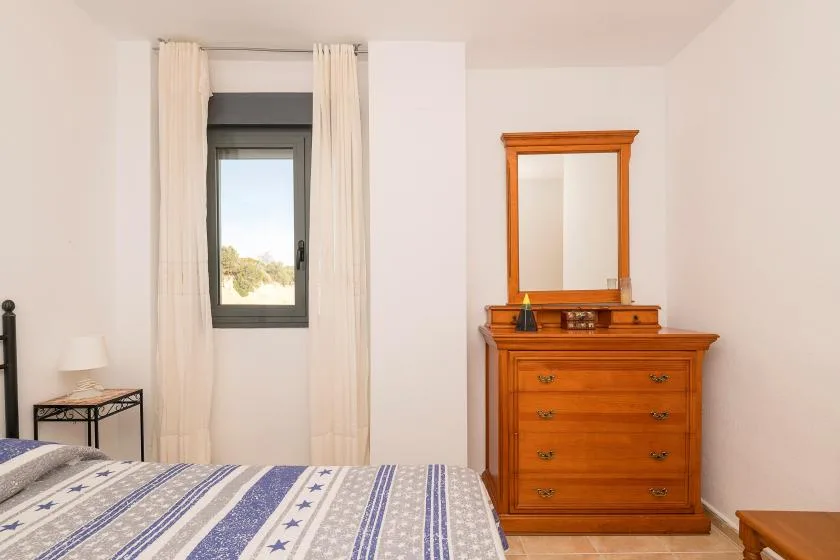 Un dormitorio con una cama estampada, una ventana y una cómoda de madera con espejo.