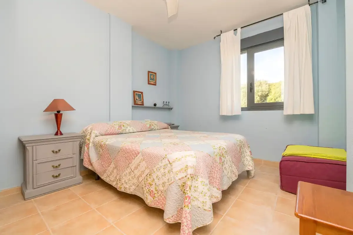 Un dormitorio con una cama junto a una ventana con cortinas blancas.