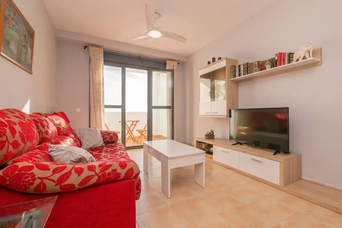 Un salón con asientos rojos, un televisor y puertas de cristal que dan a un balcón.