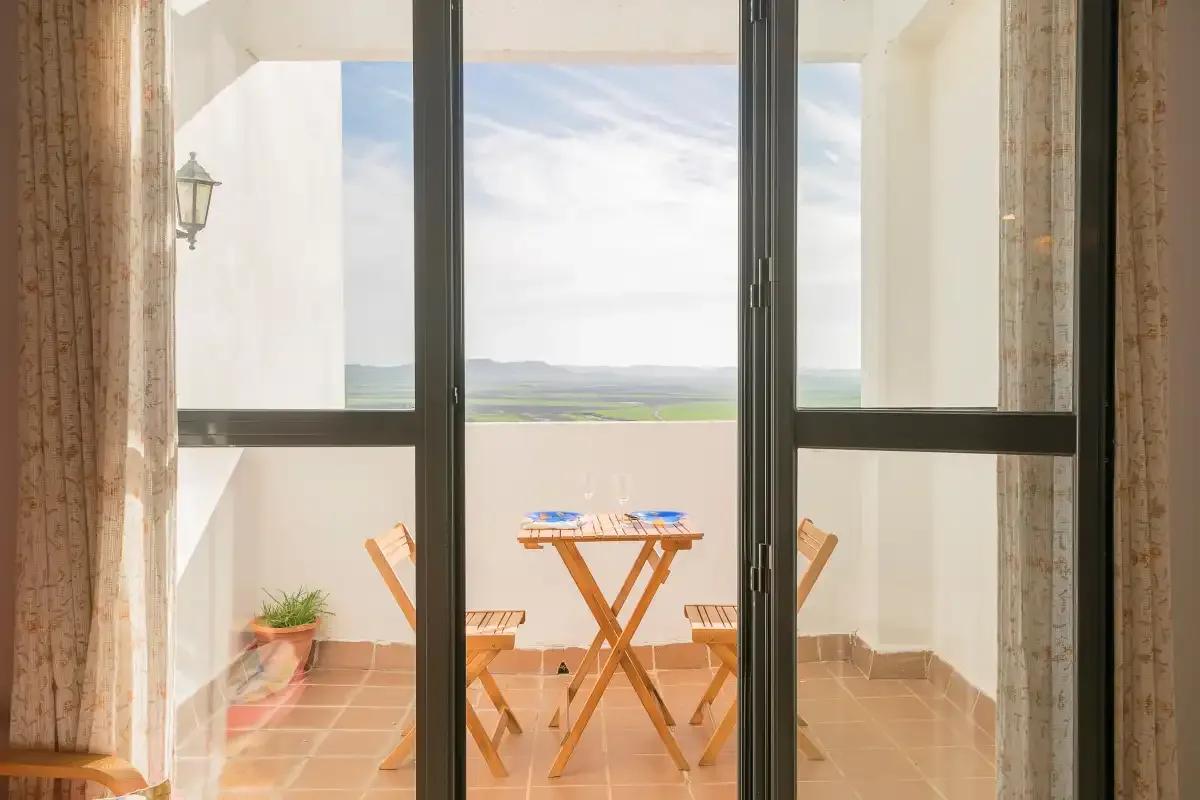 Una puerta corrediza de vidrio da a una terraza con una mesa pequeña y sillas.