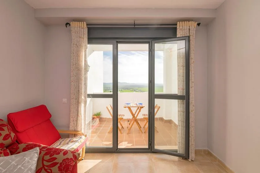 A living area opens onto a balcony through glass doors, with seating and a small table.