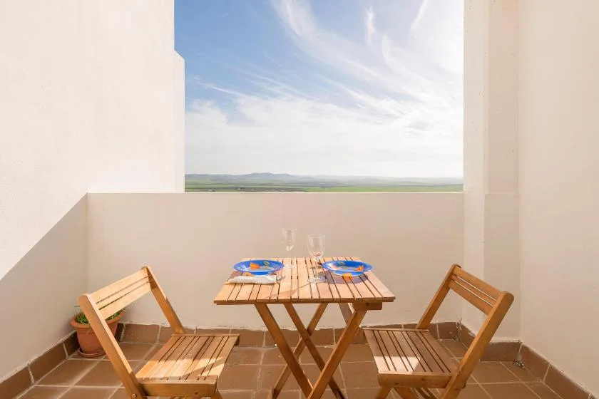A small outdoor dining area with a wooden table and chairs overlooking open countryside.