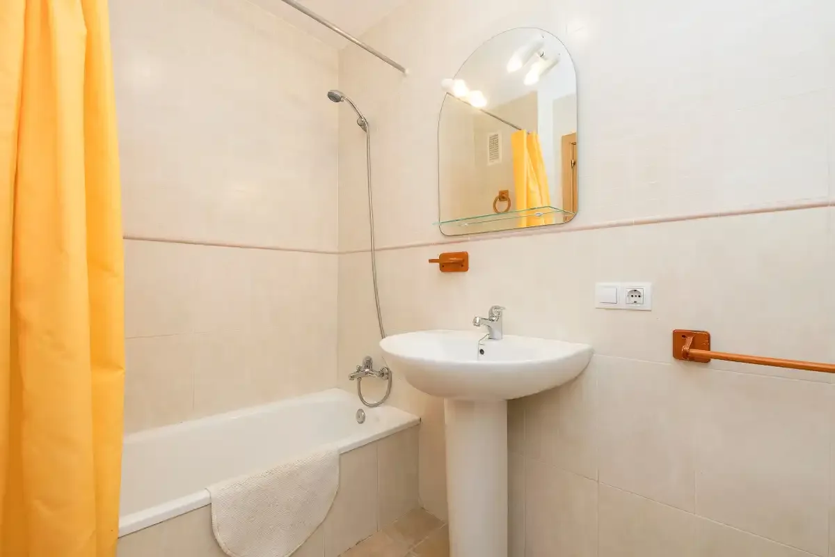 Un baño con bañera, lavabo y cortina de ducha amarilla.