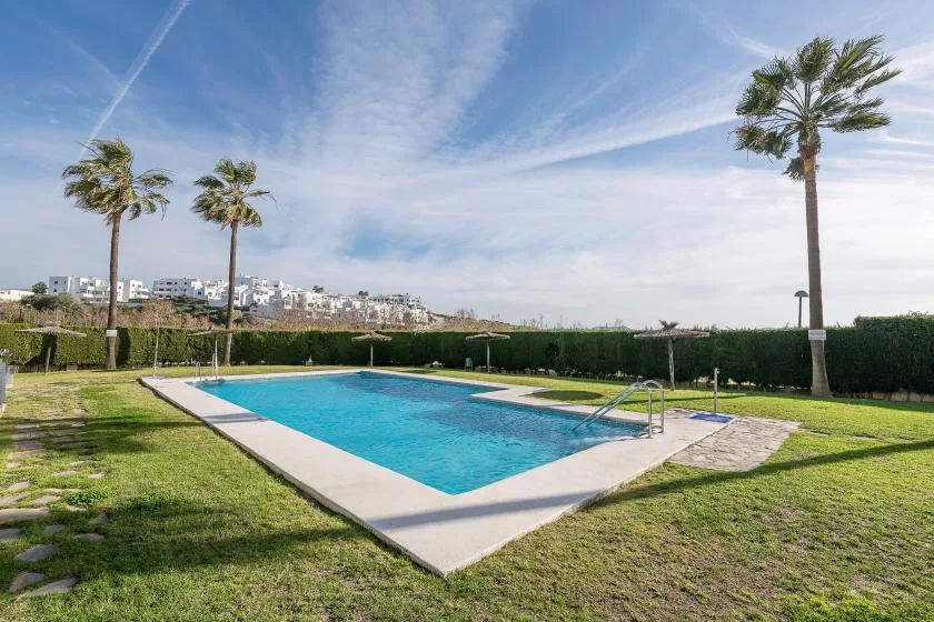 An outdoor swimming pool sits in a grassy garden beneath a clear blue sky.