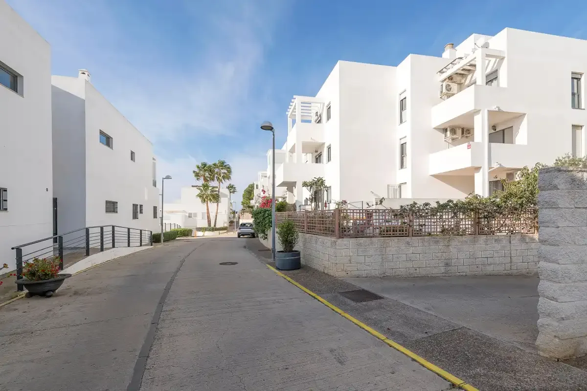 Una calle pavimentada pasa entre edificios blancos con balcones y jardineras.