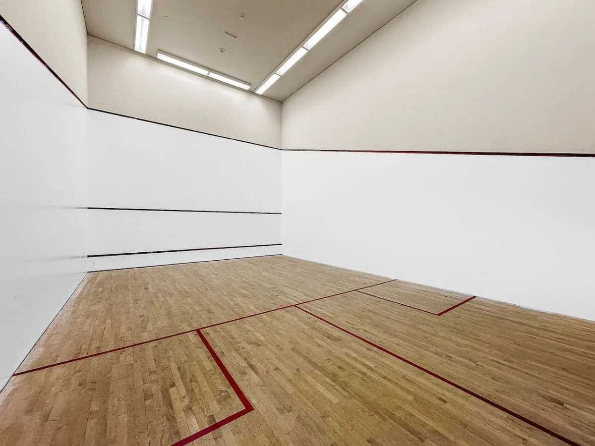 A squash court with a wooden floor and red boundary lines.