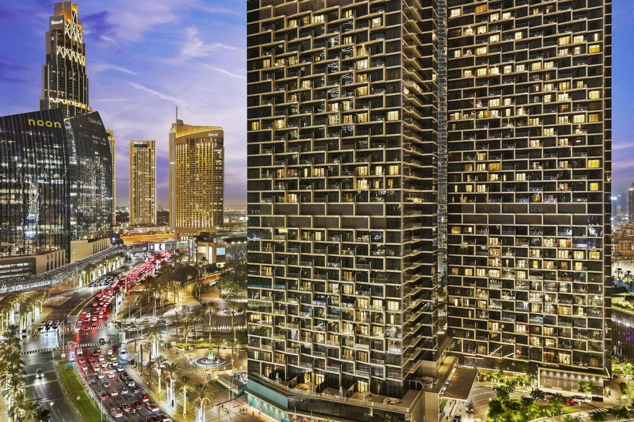 A nighttime cityscape shows illuminated high-rise buildings beside busy roads.