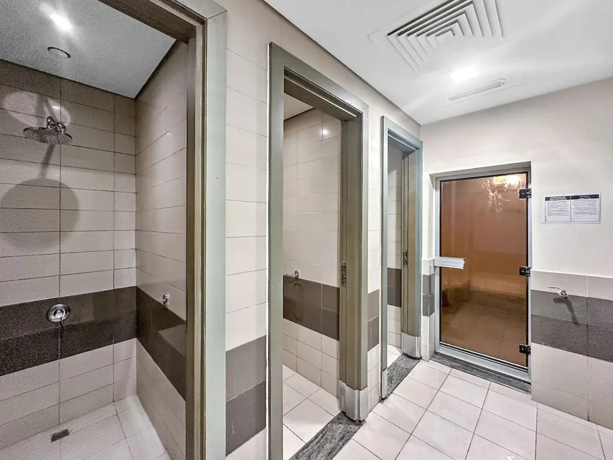 A tiled bathroom area with several shower stalls and a door at the far end.