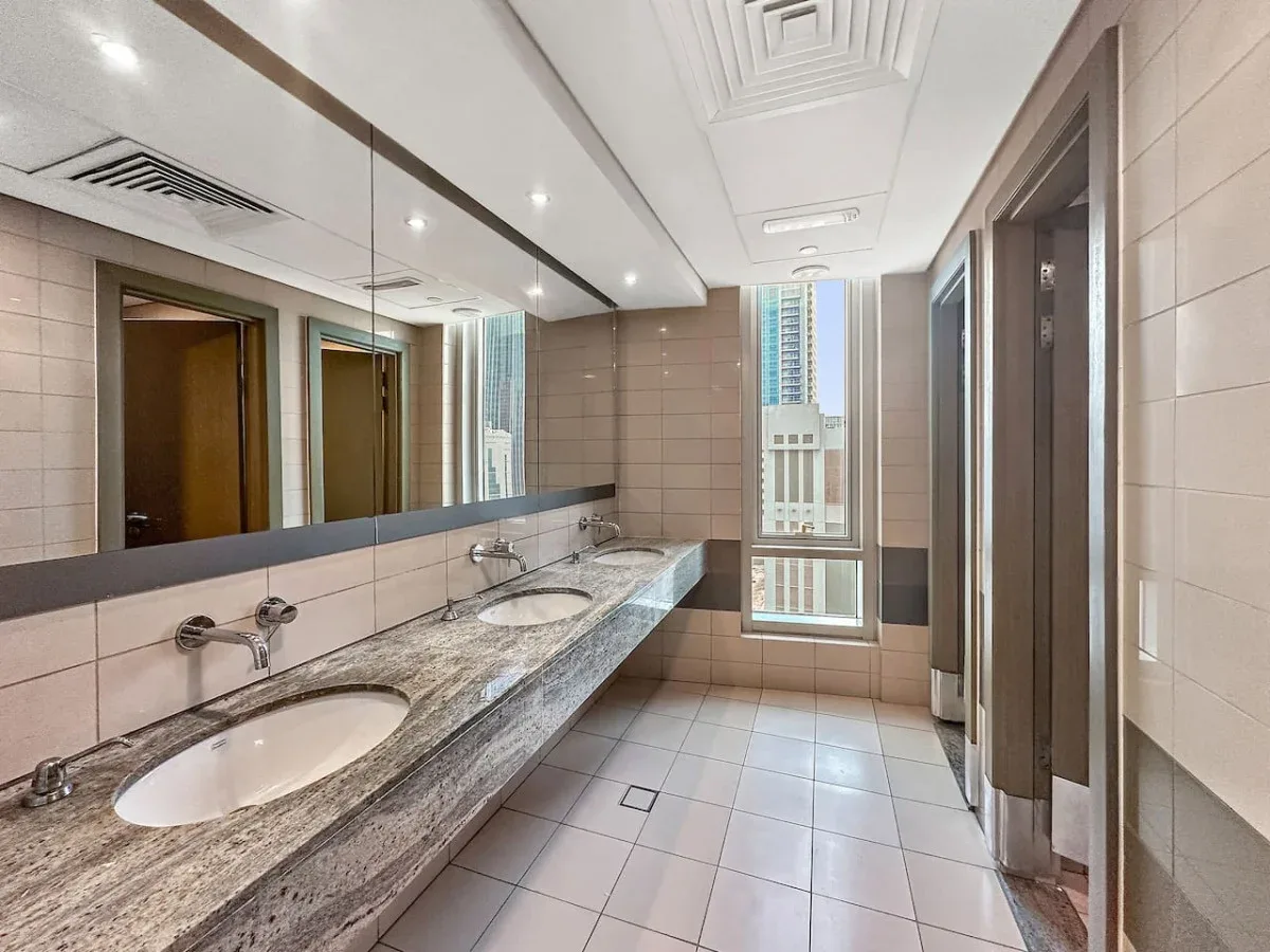 A bright bathroom with a long counter, sinks, and a large mirror.