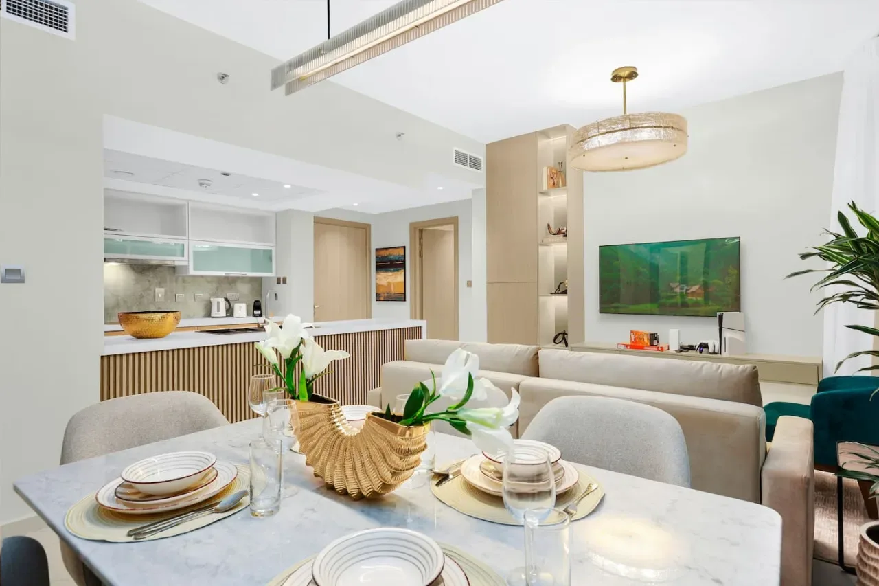 A bright open-plan living and dining area with a set table and wall-mounted television.