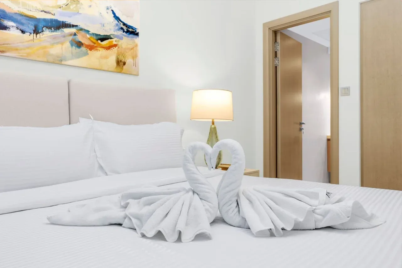 A bedroom with white bedding and towels folded into swan shapes.