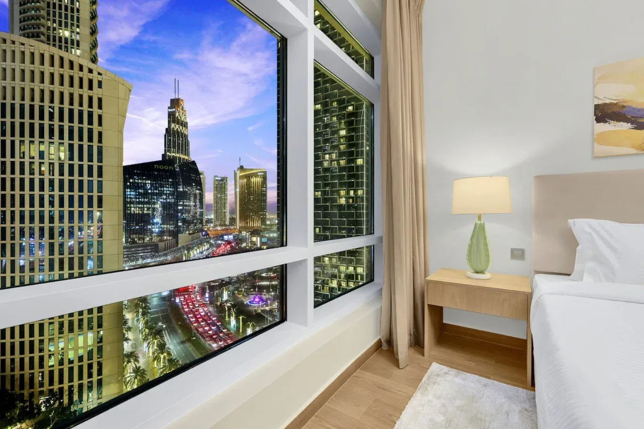 A bedroom with a large window overlooking illuminated city buildings.