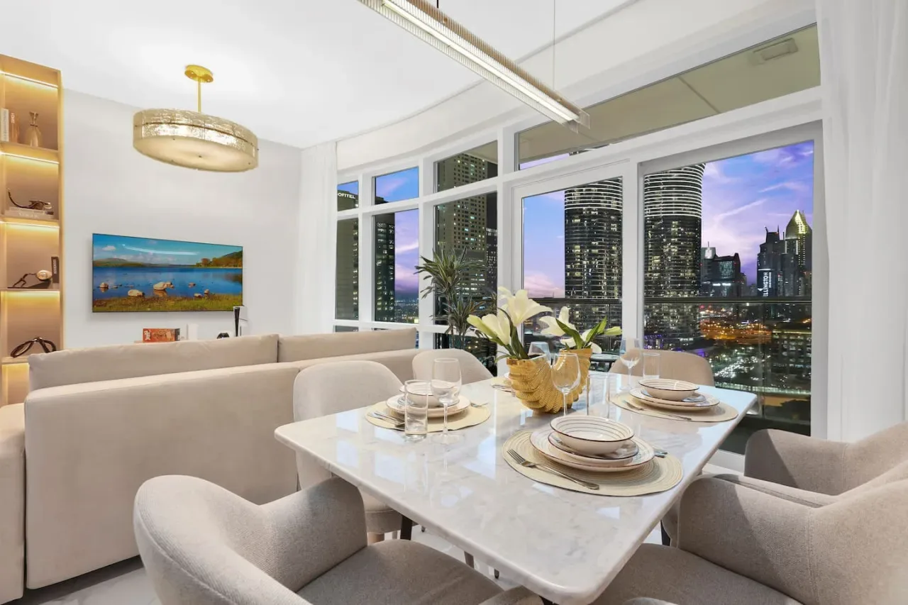 A dining area with a set table beside large windows overlooking a city skyline.