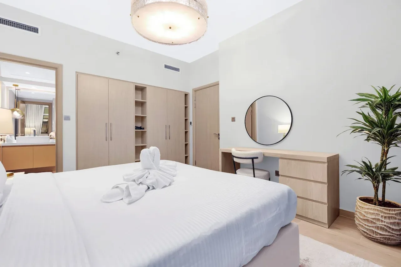 A bright bedroom with a neatly made bed and a desk beside a round mirror.