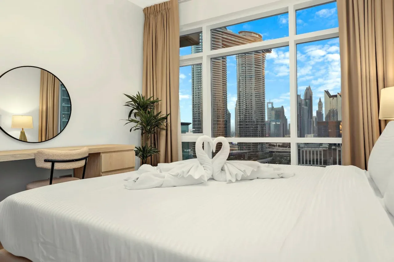A bright bedroom with a large bed facing tall windows and a city skyline.